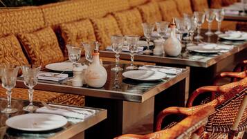 Un espace repas avec plusieurs tables dressées, chacune étant pourvue d’assiettes, de verres et d’une bouteille au centre.