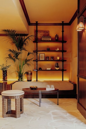 A room with a wooden bench, a round table, and a shelving unit with decorative items. - Le Mas Candille (Mougins)
