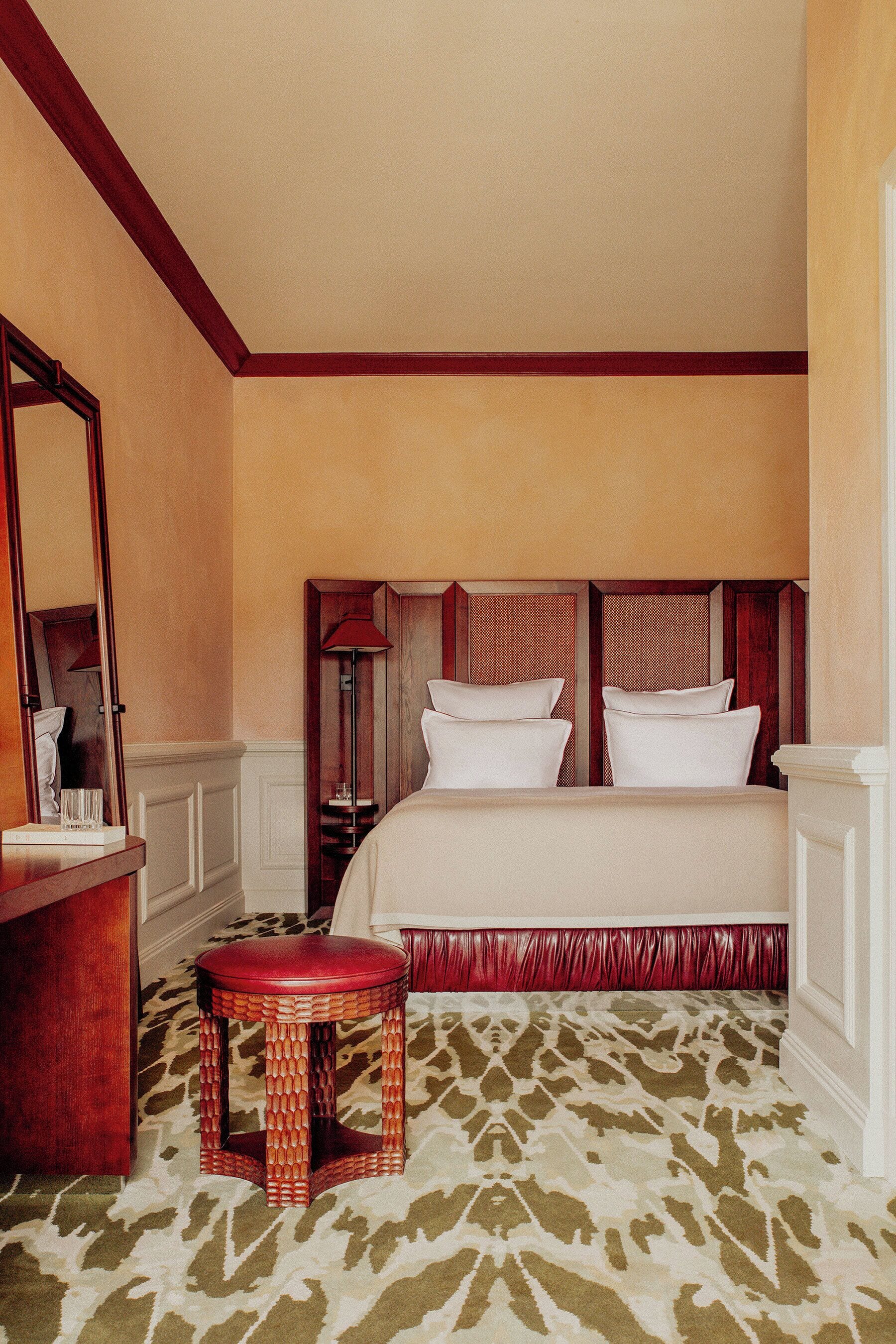 Una habitación de hotel con una cama grande, una mesita de madera, un espejo y una alfombra estampada.