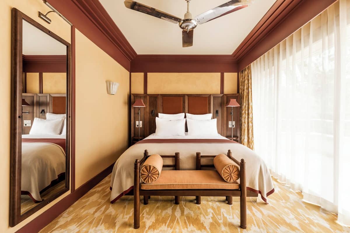 A hotel room with a large bed, a ceiling fan, a wooden bench, and a large mirror.
