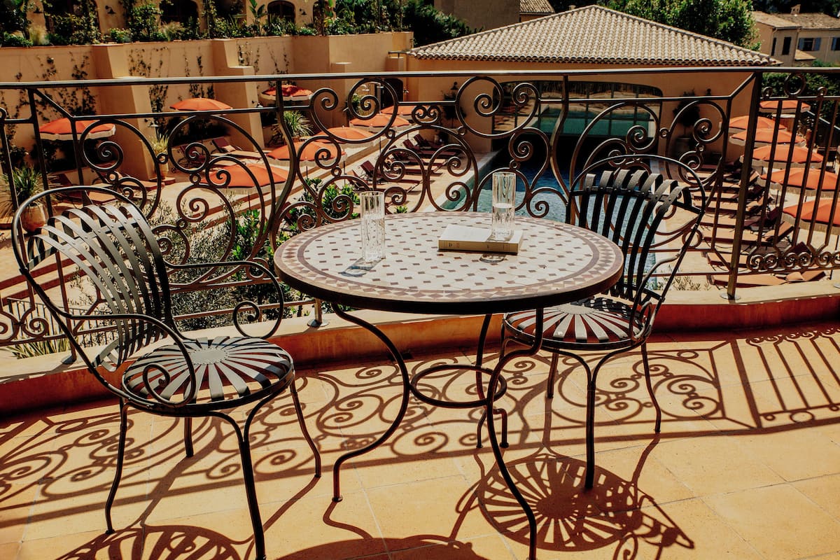 A round metal table with chairs and a glass on a tiled patio with decorative metal railings.
