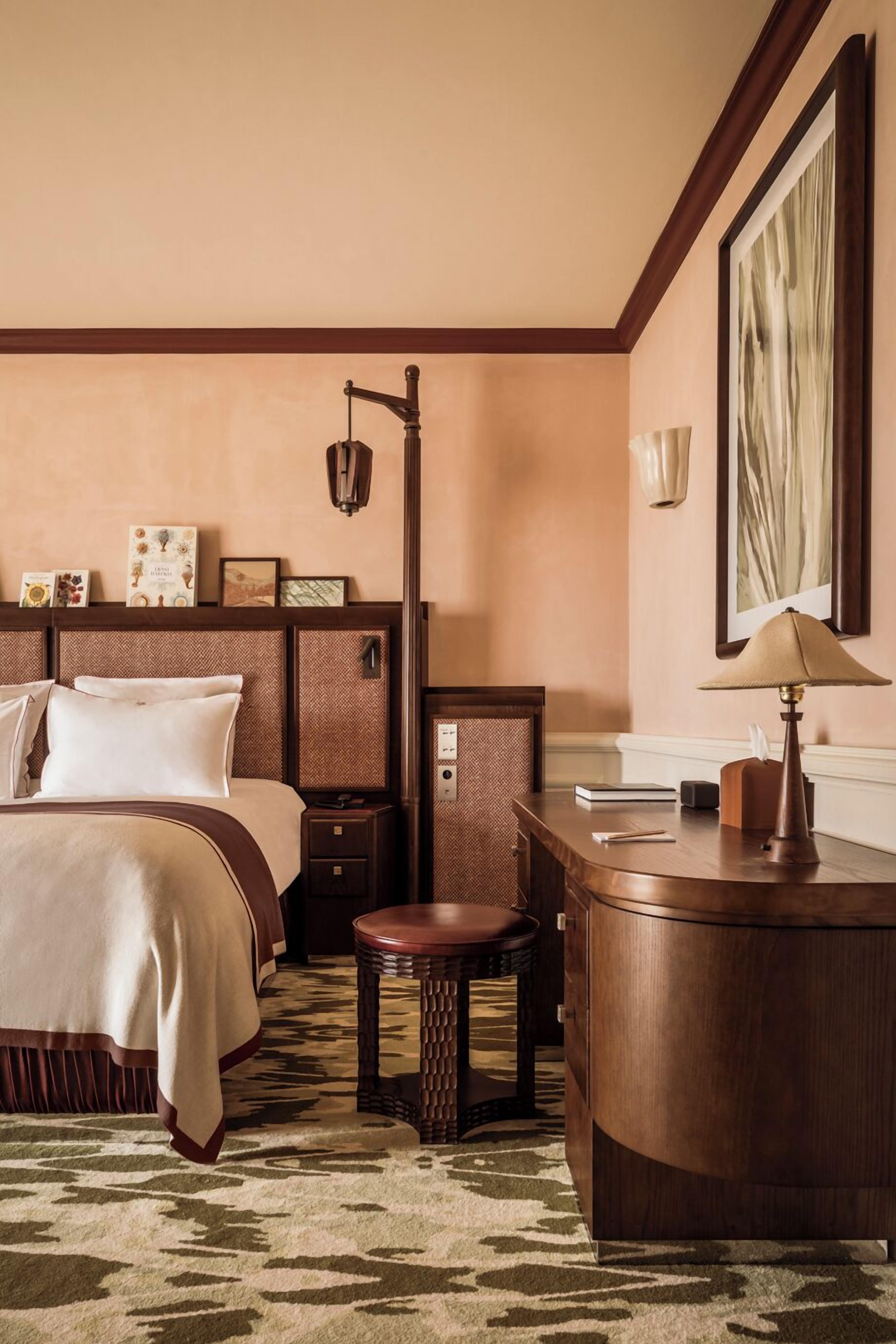 Een hotelkamer met een bed, een bureau, een stoel, een lamp en een ingelijste foto aan de muur.