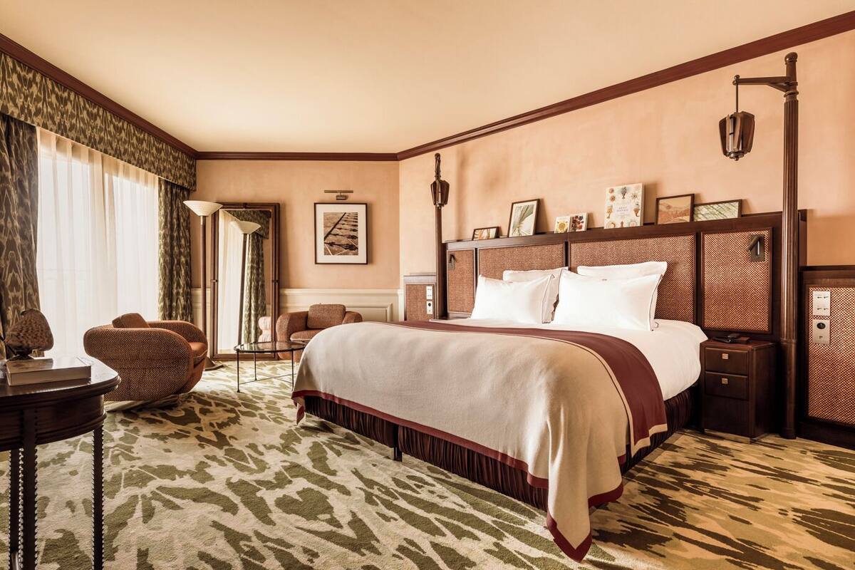 A hotel room with a large bed, a chair, a small table, and a lamp.