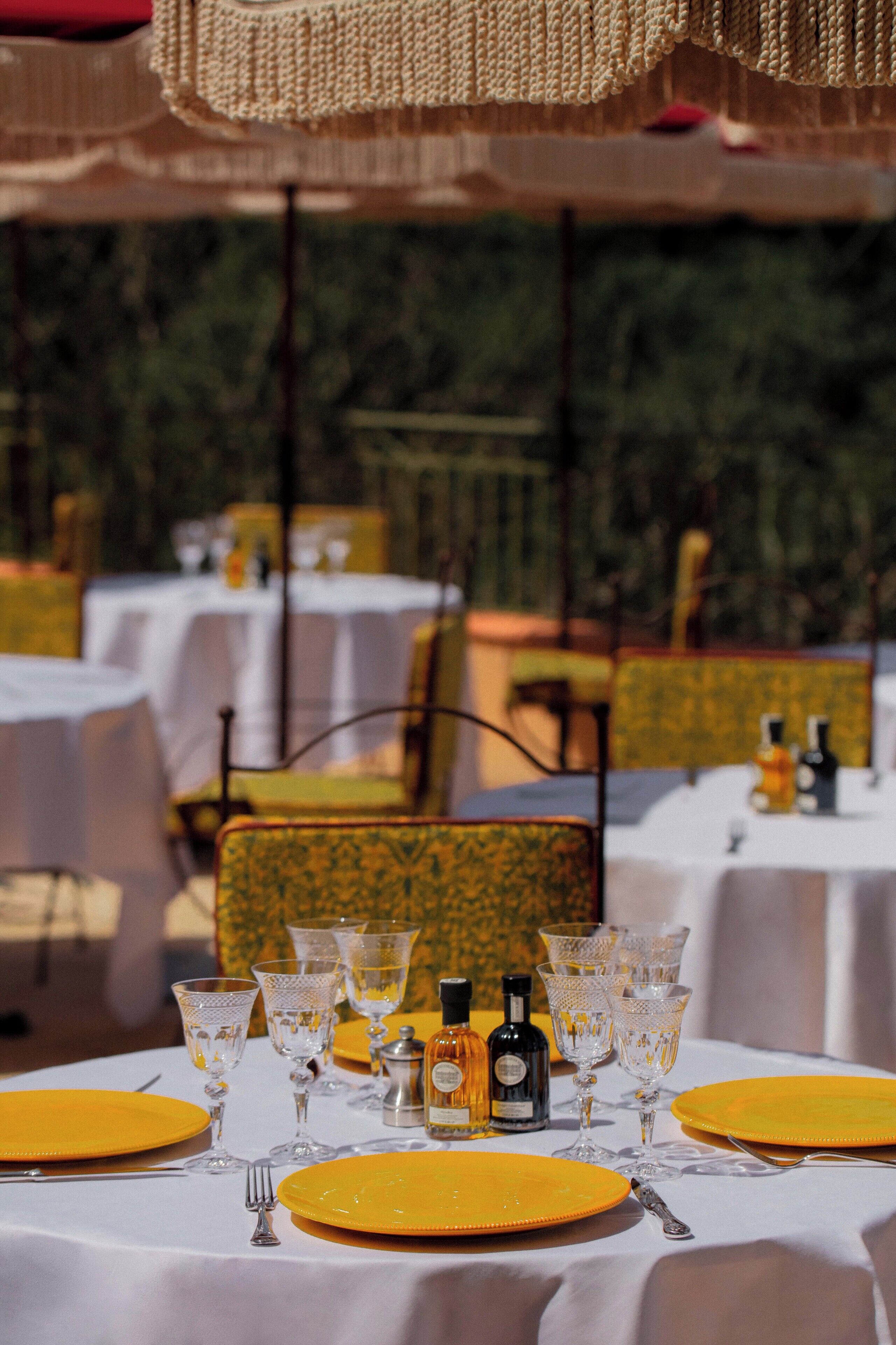 An outdoor dining area with tables set for a meal, featuring yellow plates and clear glassware.