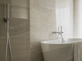 Een moderne badkamer met een vrijstaand bad, een douchekop en een handdoek aan de muur.