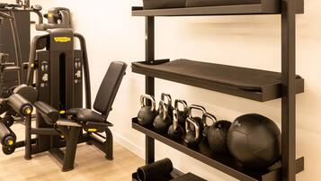 Un gimnasio con equipo de ejercicio, una banca, kettelbells y un peso en un estante.