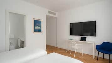 Una habitación de hotel moderna con una cama grande, un escritorio con una computadora portátil, un televisor y una silla.