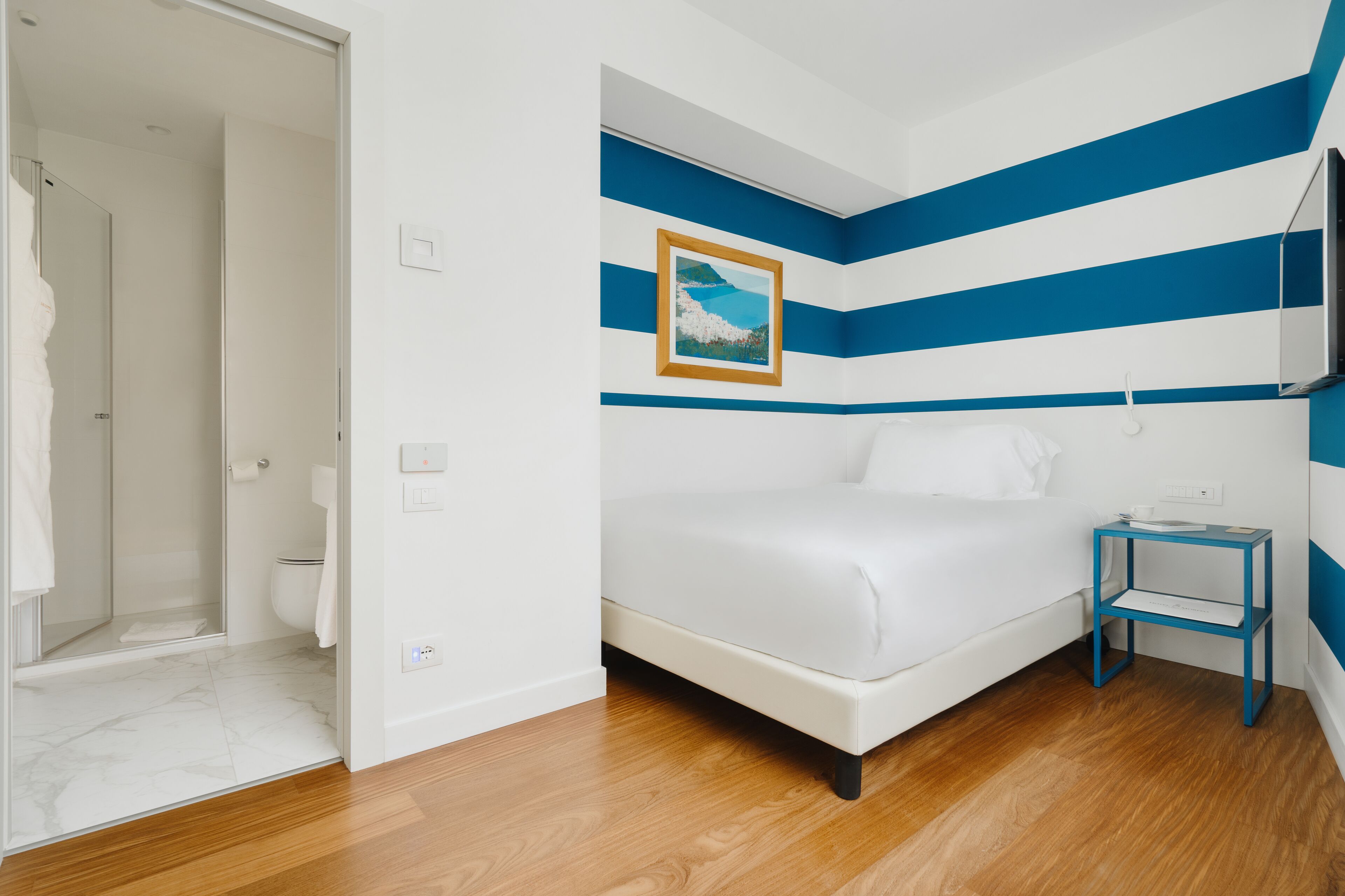 Une chambre à coucher comprenant un lit, une table de chevet, un tableau et un espace douche.
