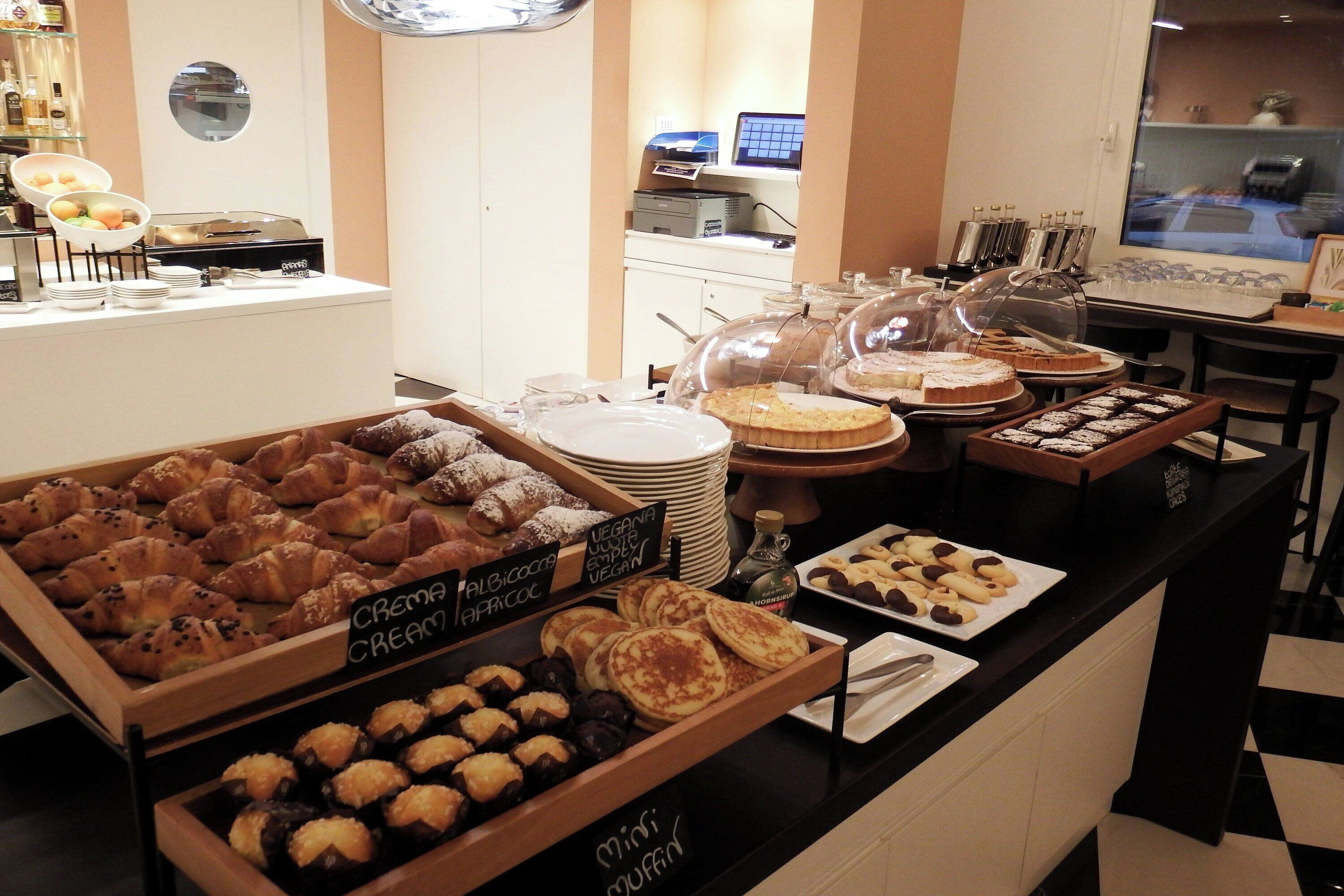 Un bufé con diversas opciones de panadería y pastelería, incluyendo croissants, muffins pequeños y tartas.