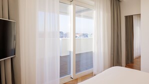 Habitación de hotel con una cama grande, televisión y puerta corrediza de vidrio a un balcón.
