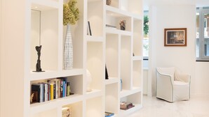 Un interior moderno con una estantería blanca que exhibe libros y objetos decorativos, una silla blanca y un suelo de mármol.