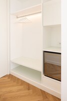 A white closet with shelves and a hanging rod, a wooden herringbone floor, and a built-in oven.