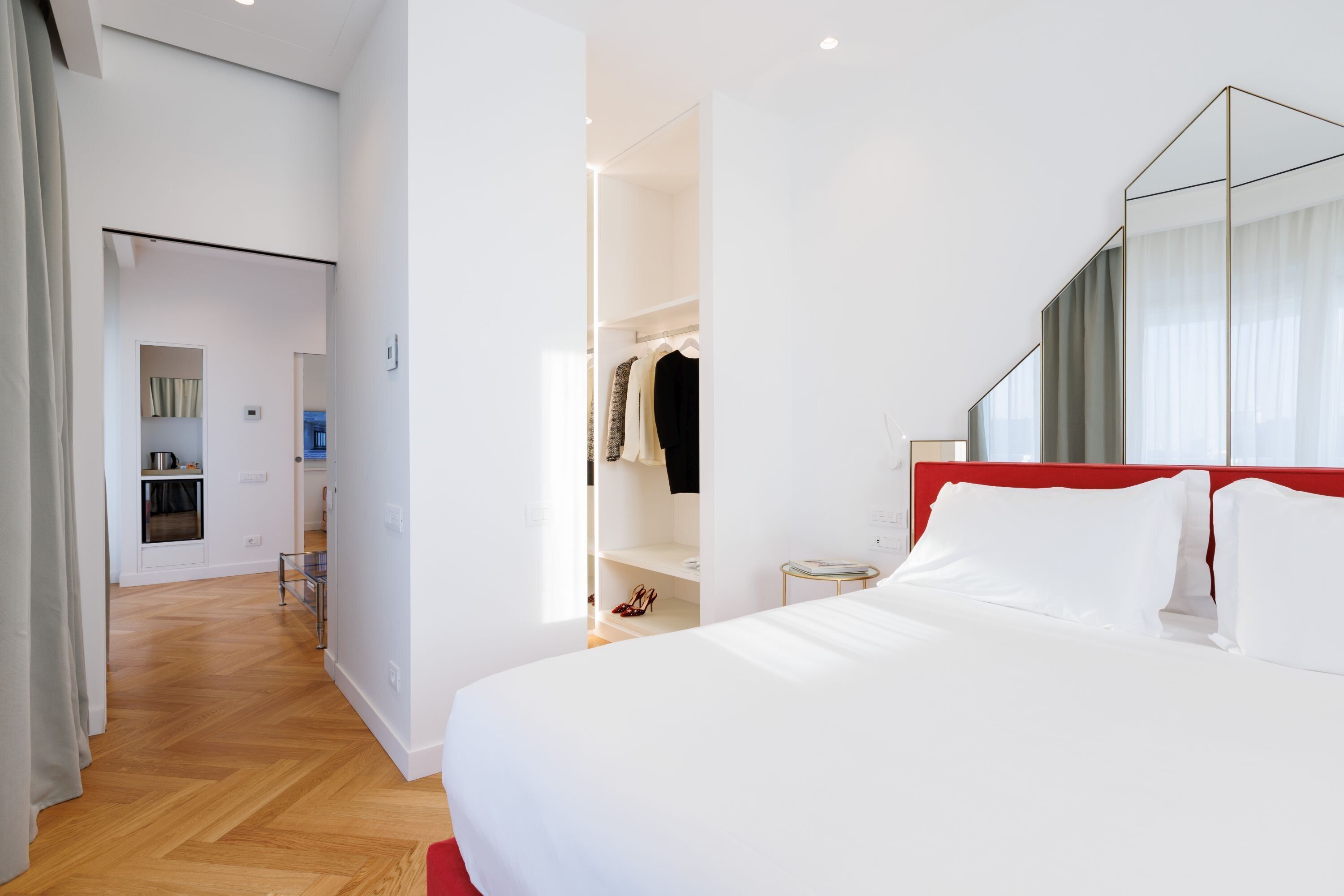 A modern hotel room with a large bed, a red headboard, and a walk-in closet.
