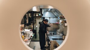 Un chef en una cocina profesional con electrodomésticos de acero inoxidable y un ventanal circular.