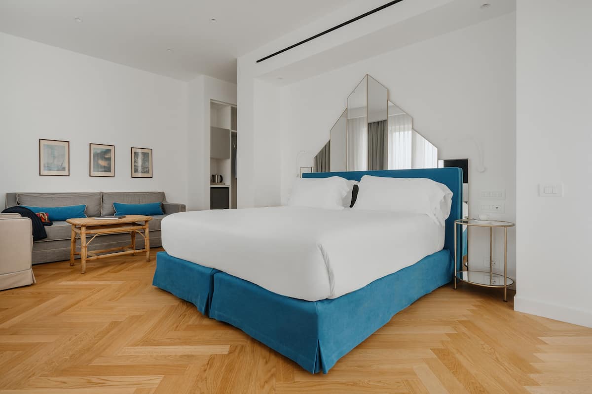 A modern hotel room with a large bed, a sofa, a small table, and a mirror.
