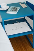 Een blauwe nachtkastje met een witte kop, schotel, lepel, een boek met de titel 'Gio Poni e Milano' en een tas van 'Hotel Morfeo Milano'.