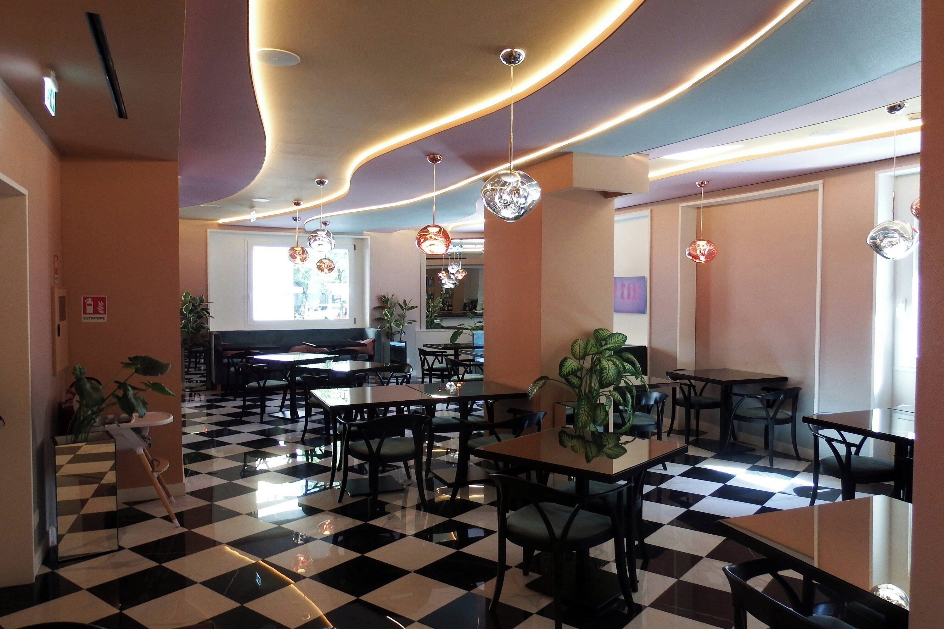 Un vestíbulo de hotel con suelo a cuadros, varias mesas y sillas, luces de techo y una planta.