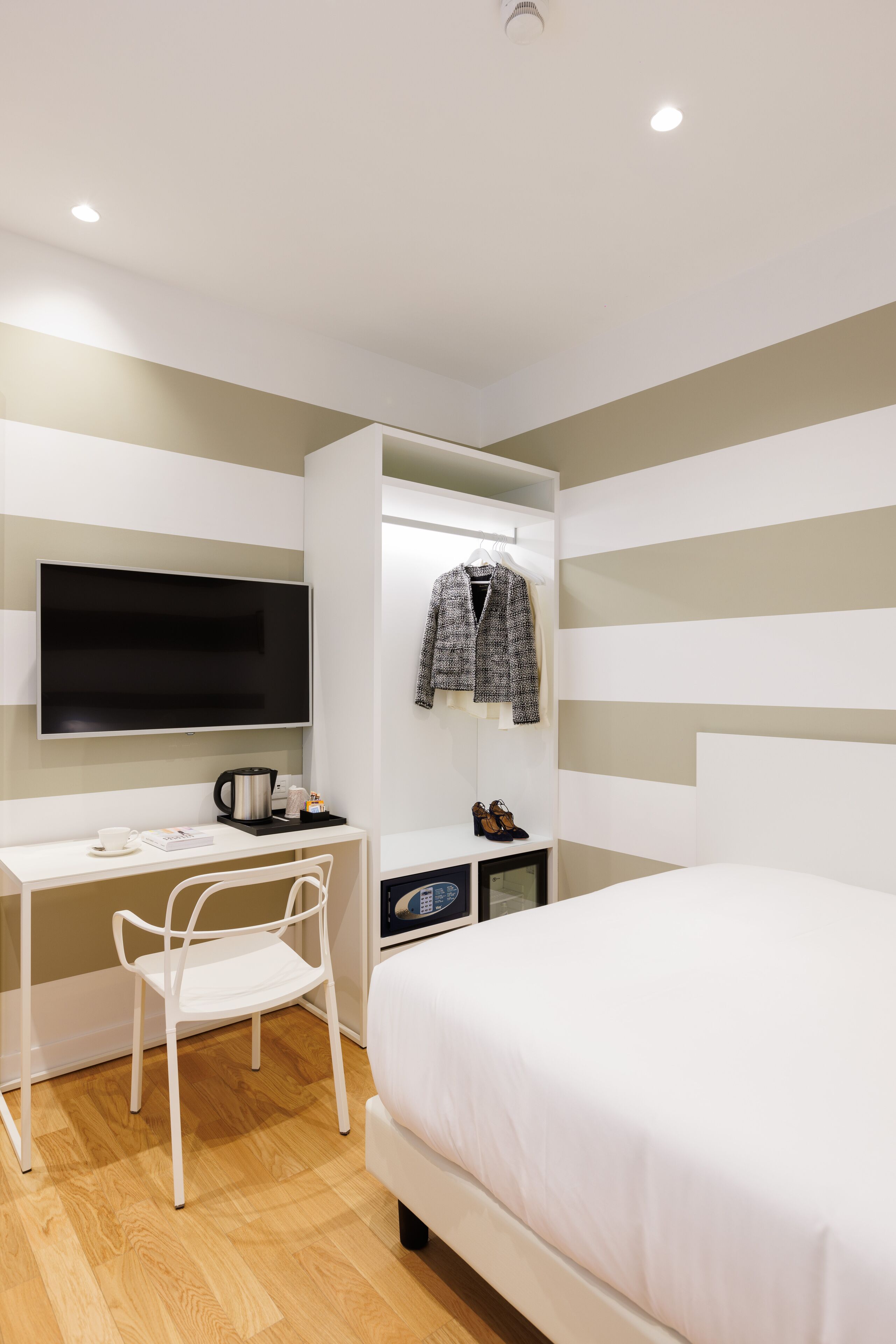 A modern bedroom with a bed, a desk, a chair, a TV, and a wardrobe.