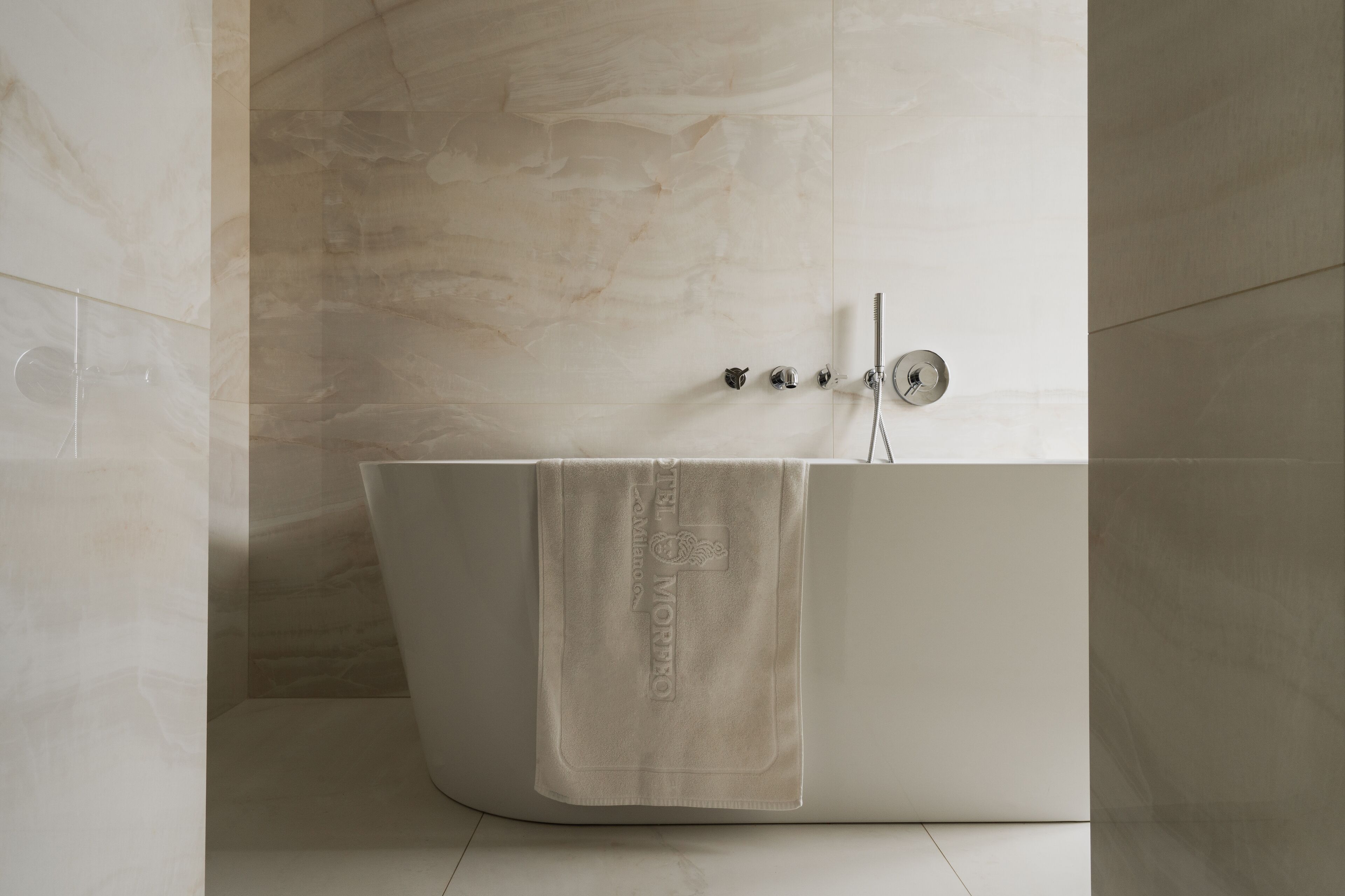 Un bagno moderno con una vasca freestanding, un asciugamano appeso e una parete in marmo.