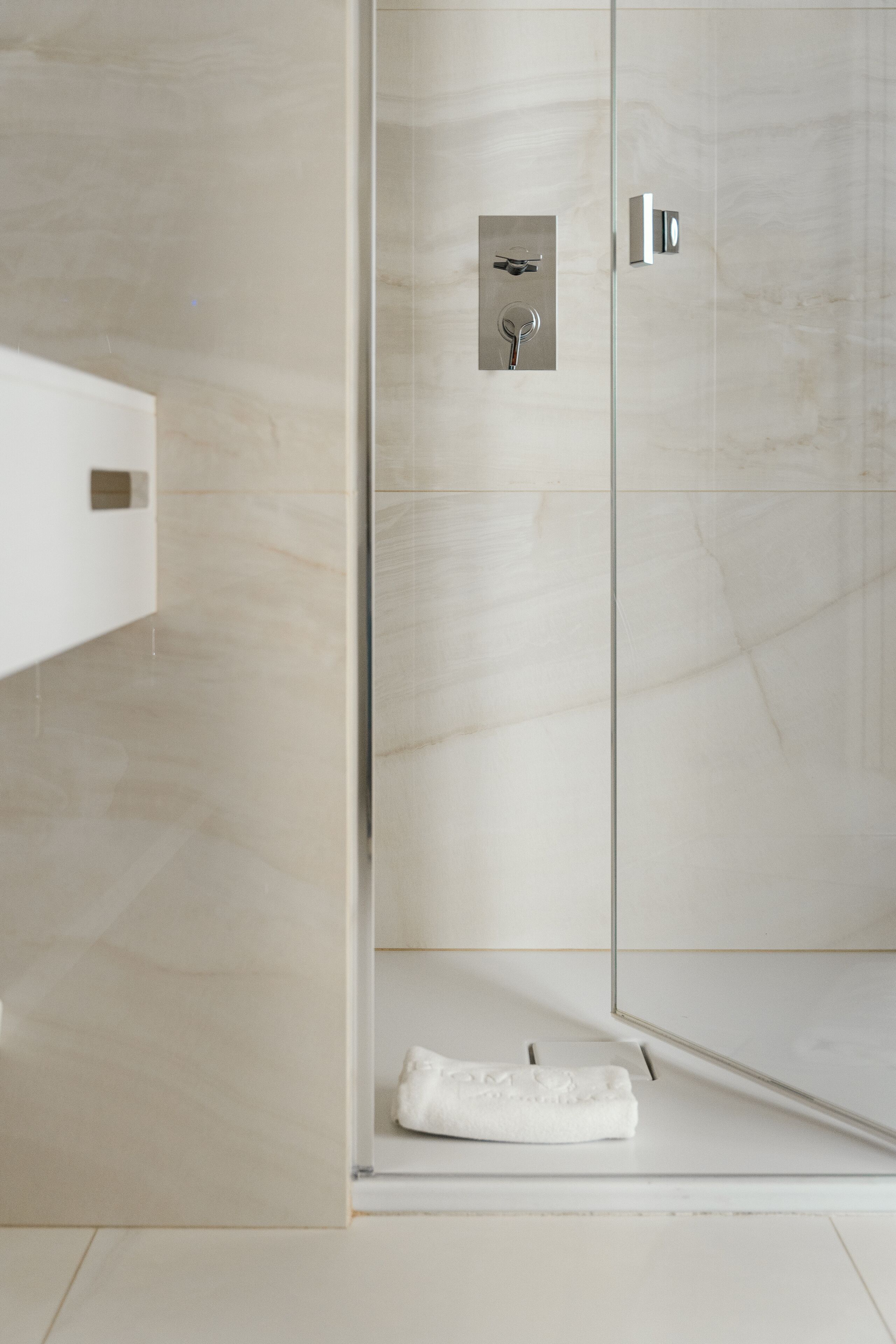 A modern bathroom with a glass shower enclosure, a white towel on the floor, and a minimalist design.