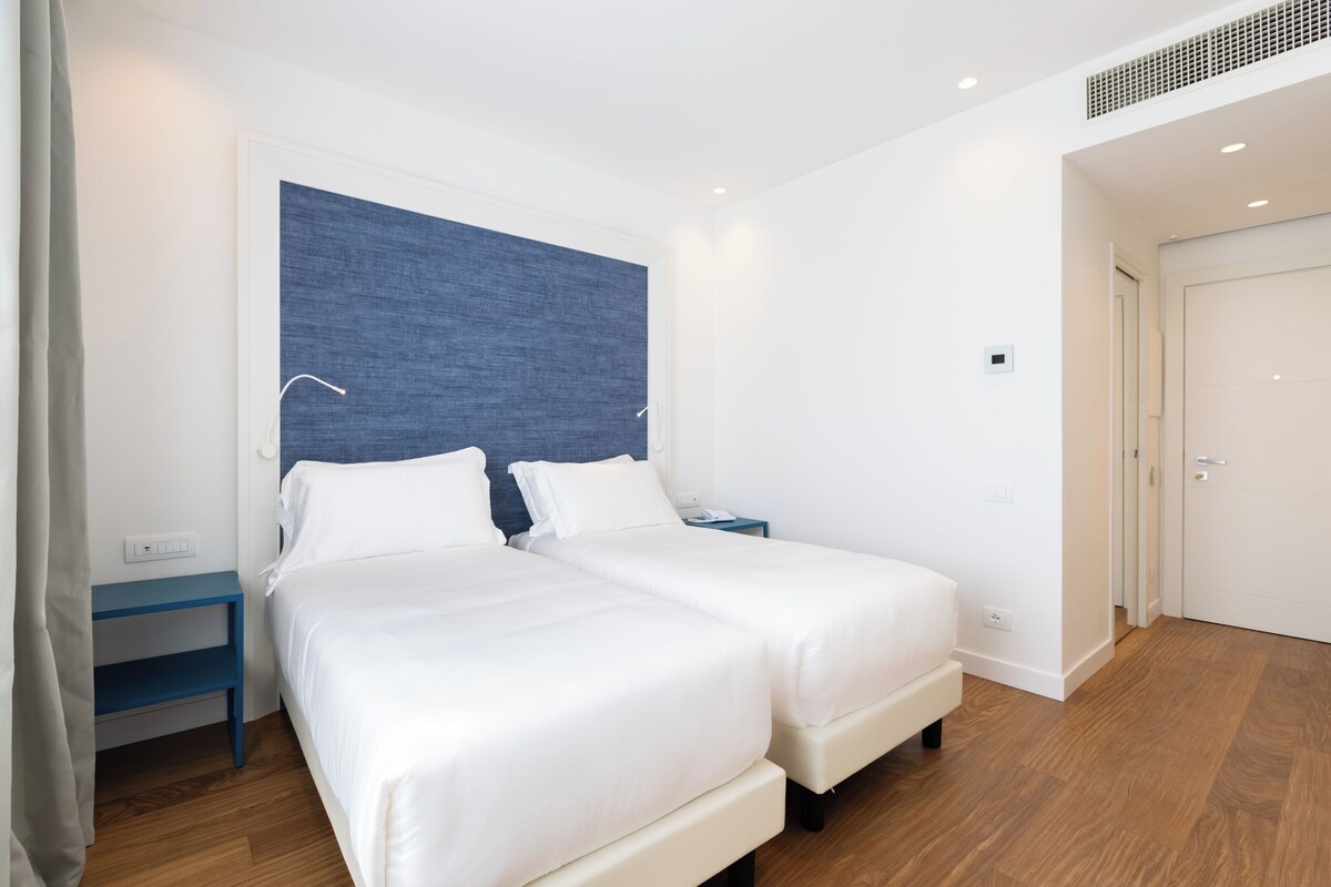 Ein modernes Hotelzimmer mit zwei Betten, einer blauen Akzentwand und Holzboden.