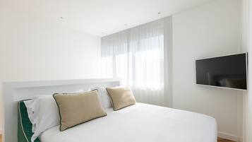 Une chambre d’hôtel moderne dotée d’un grand lit, d’un téléviseur à écran plat fixé au mur et d’une grande fenêtre avec des rideaux légers.