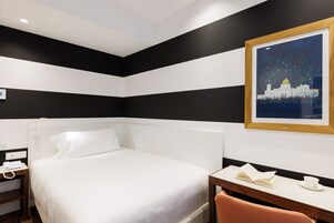 Een hotelkamer met een bed, nachtkastje en een bureau met stoel.