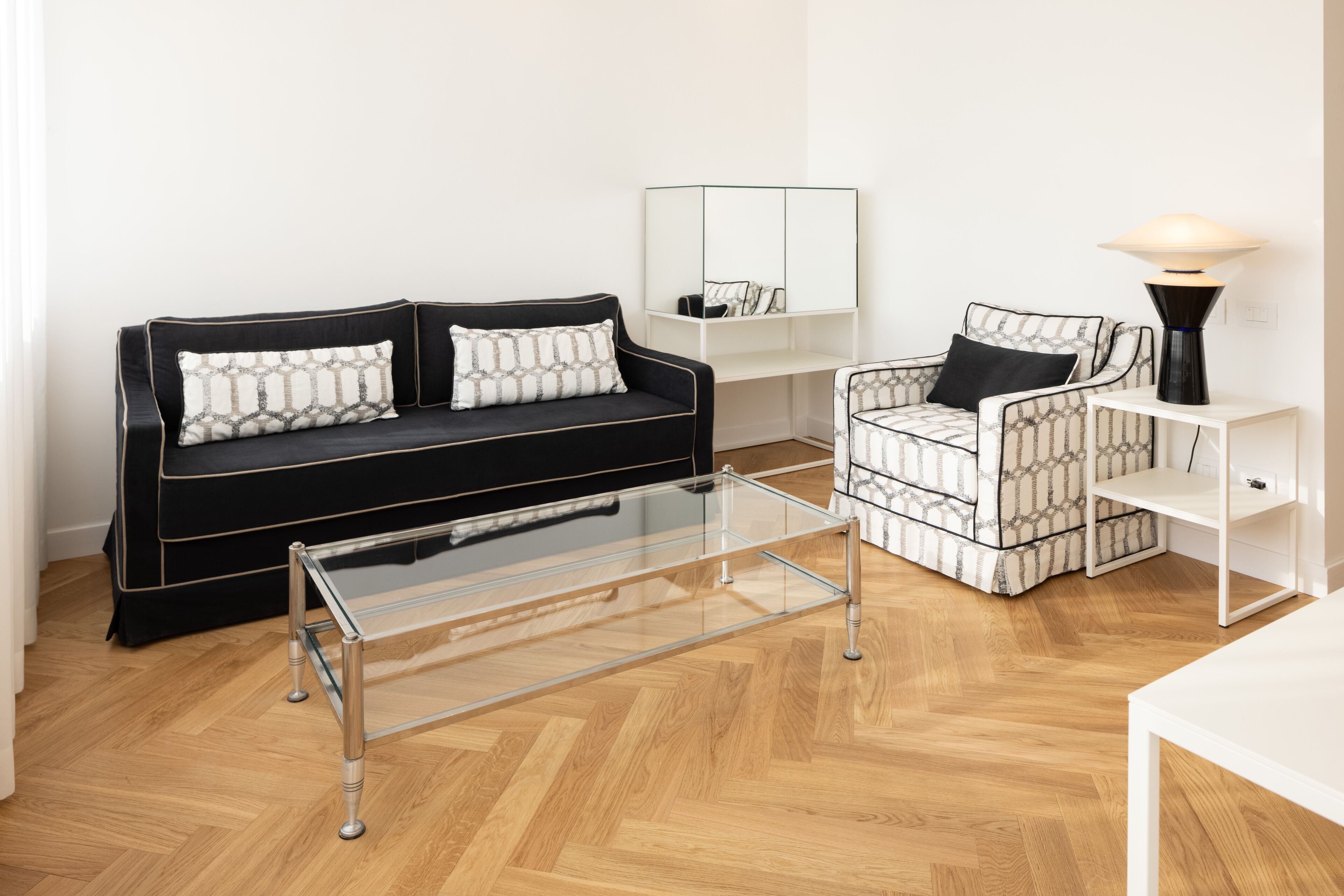 Una sala de estar moderna con un sofá negro, un sillón estampado y una mesa de centro de vidrio.