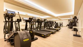 Ein Fitnessraum mit mehreren Laufbändern und Crosstrainern, Holzboden und modernem Deckenbau.