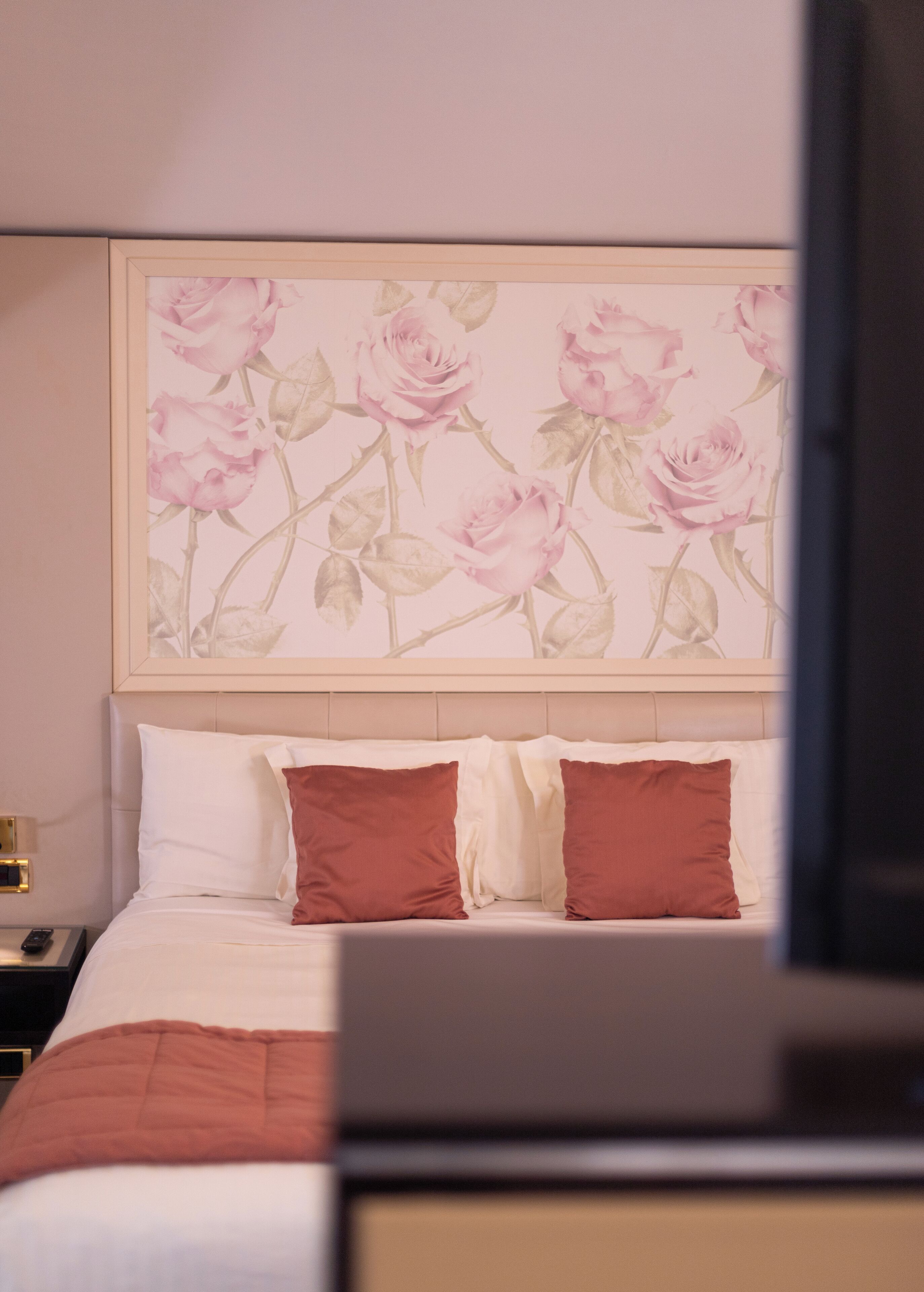 Une chambre d’hôtel avec un lit, deux oreillers, une table de chevet et un mur orné d’un tableau représentant des motifs floraux.