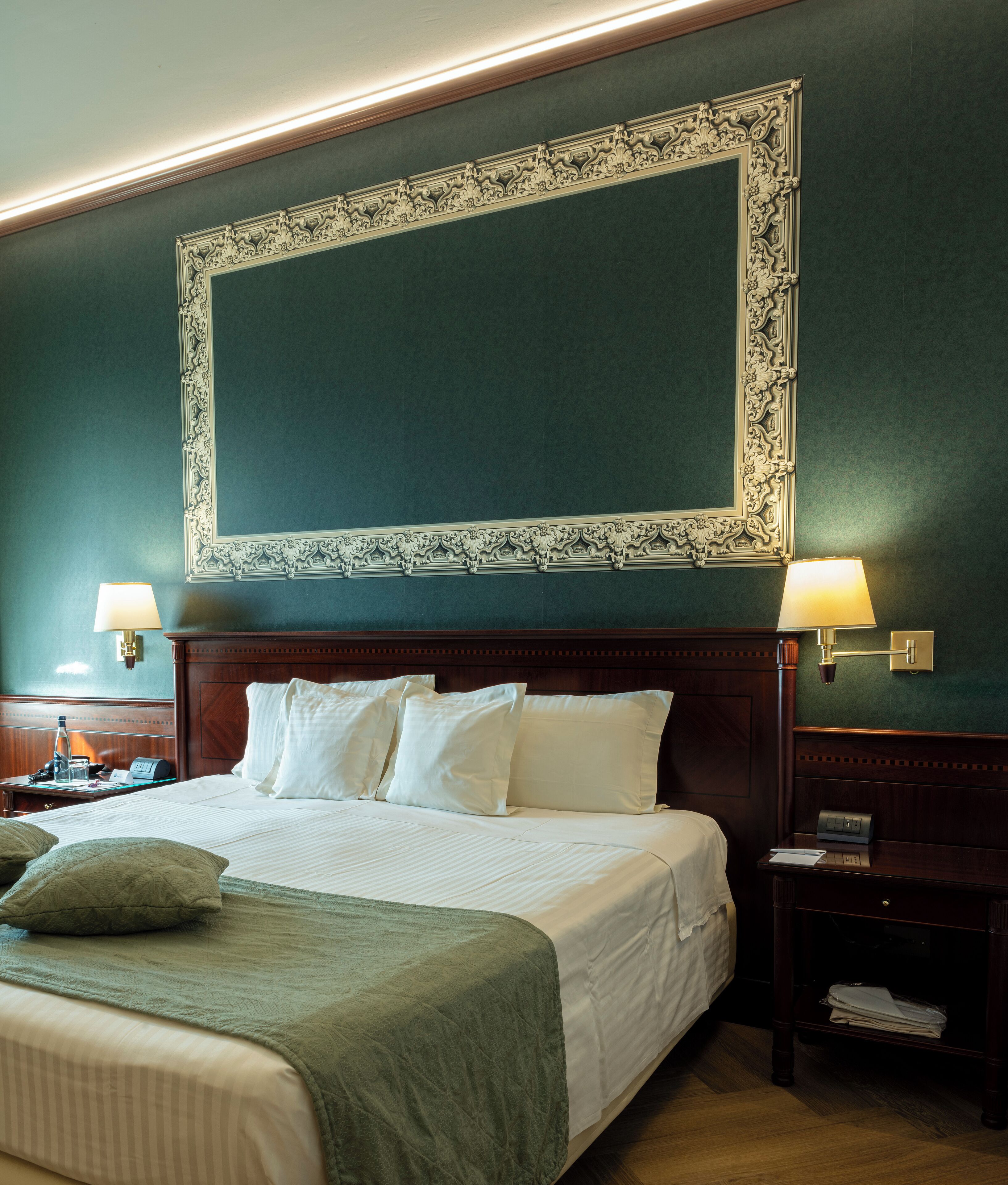Habitació d'hotel amb un llit gran, dues taules de nit i un mirall gran i ornamentat sobre el llit.