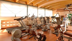 A gym with various exercise machines, wooden beams on the ceiling, and a large window providing natural light. - c-hotels Concorde (Milan)