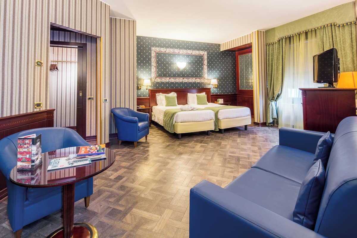 Ein Hotelzimmer mit Doppelbett, zwei Nachttischen, einem Fernseher, einem Schreibtisch mit Stuhl und einem Sofa.