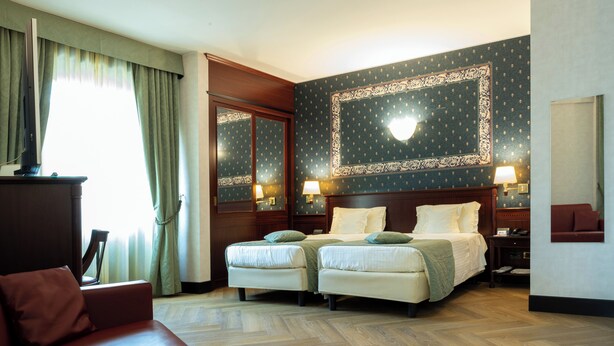 Habitación de hotel con una cama doble, dos mesitas de noche con lámparas, un televisor, un cabecero de madera y un espejo grande.