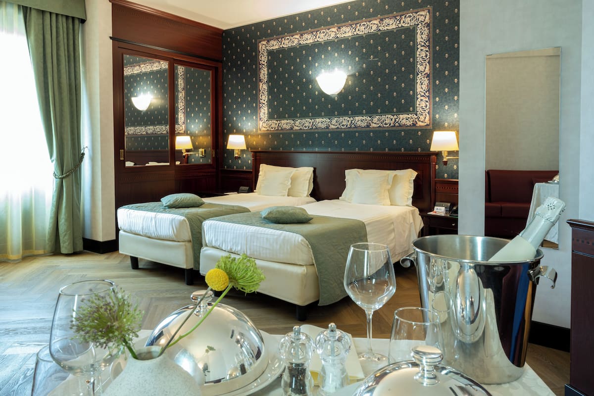 Ein Hotelzimmer mit zwei Betten, einem Esstisch gedeckt mit Geschirr und einem großen Metallbehälter.
