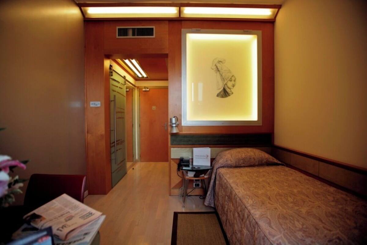 Ein Hotelzimmer mit Bett, Schreibtisch und einem an der Wand hängenden Kunstwerk.
