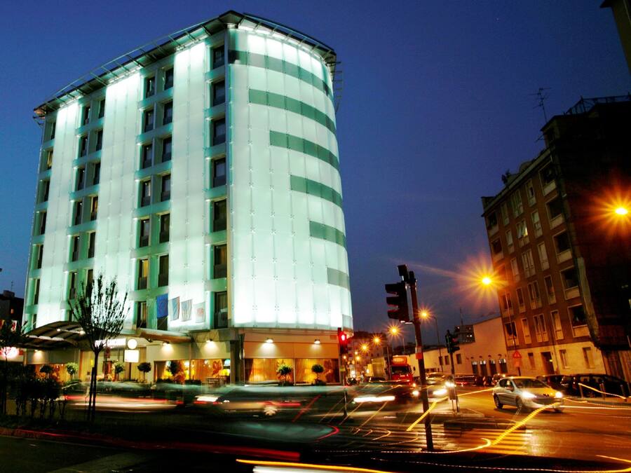 A multi-story hotel with a modern design, featuring a curved facade and illuminated windows.