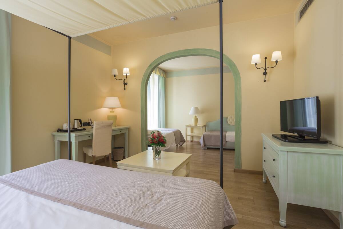 Une chambre d’hôtel équipée d’un lit, d’un bureau, d’une chaise, d’une télévision et d’une petite table sur laquelle se trouve un vase de fleurs.