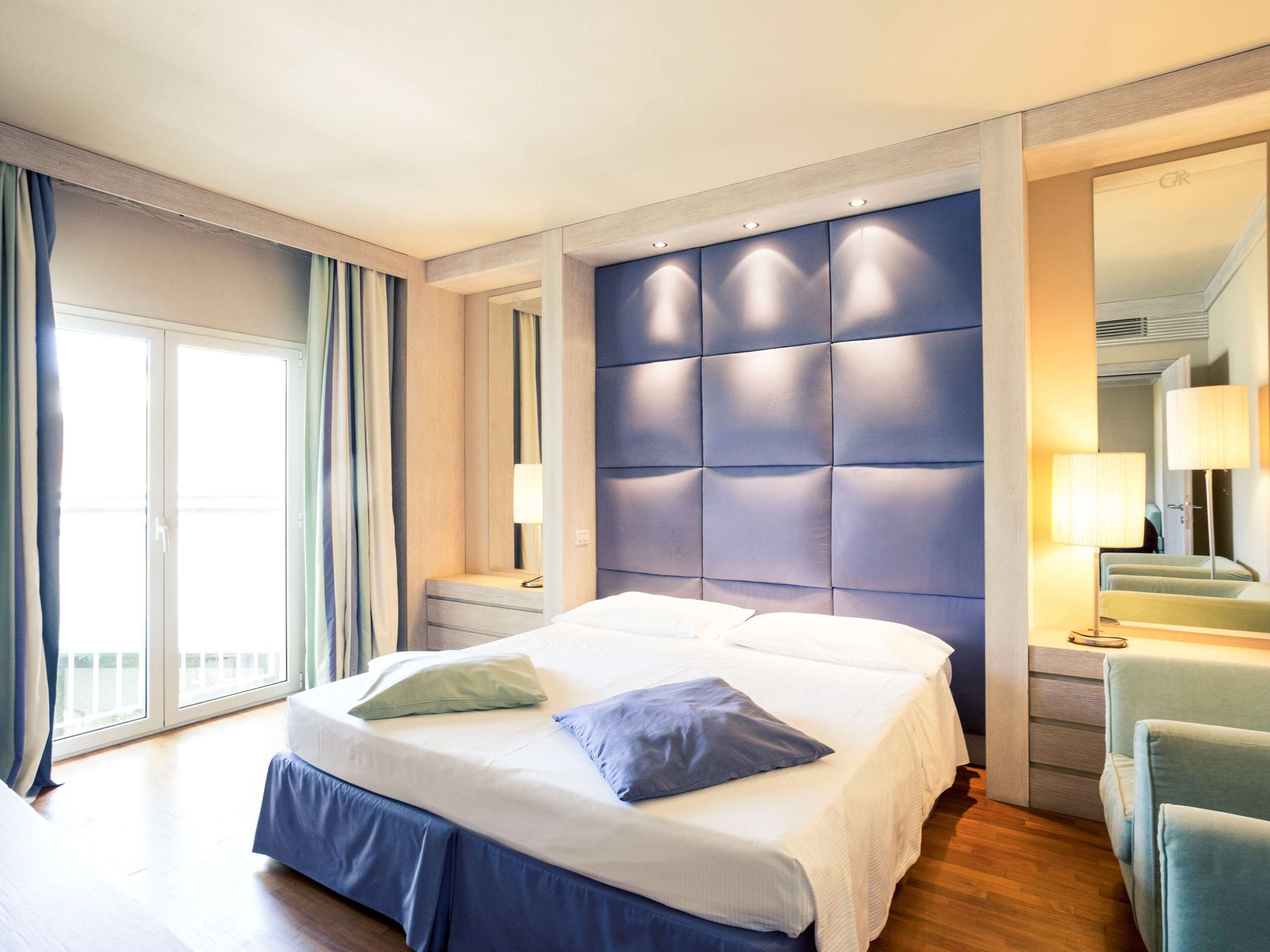 A hotel room with a large bed, a nightstand, a chair, and a view of the outdoors.