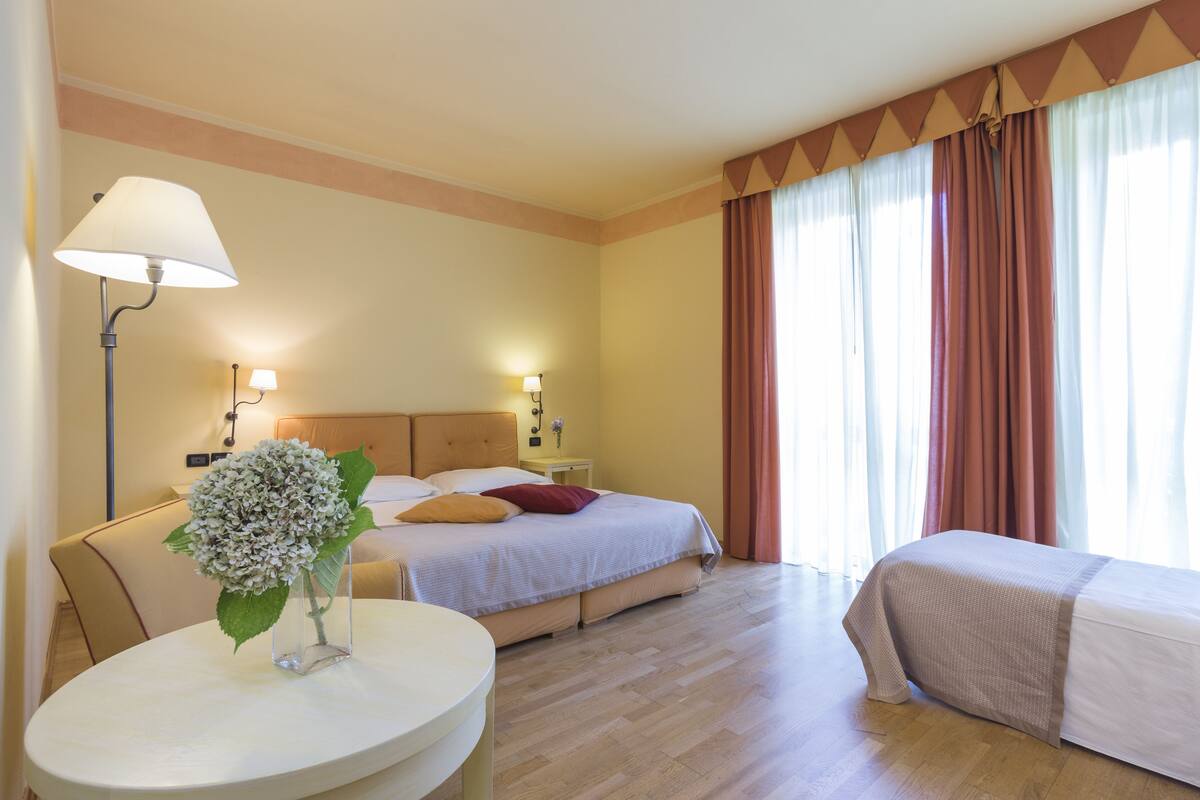 Une chambre d’hôtel avec un lit, des tables de chevet, une lampe et un vase avec des fleurs.