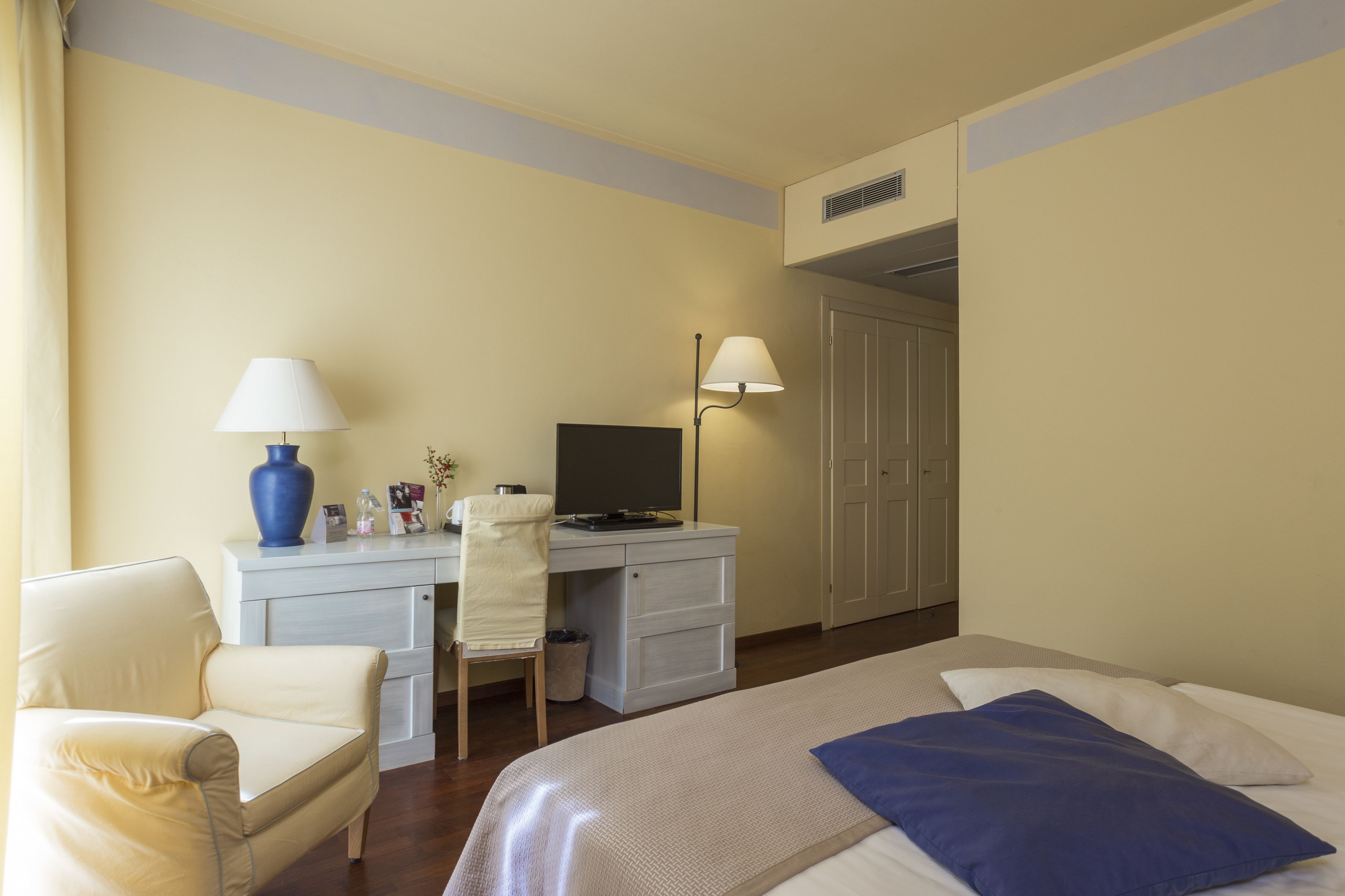 Una habitación de hotel con una cama, un escritorio con computadora, una silla y una lámpara.