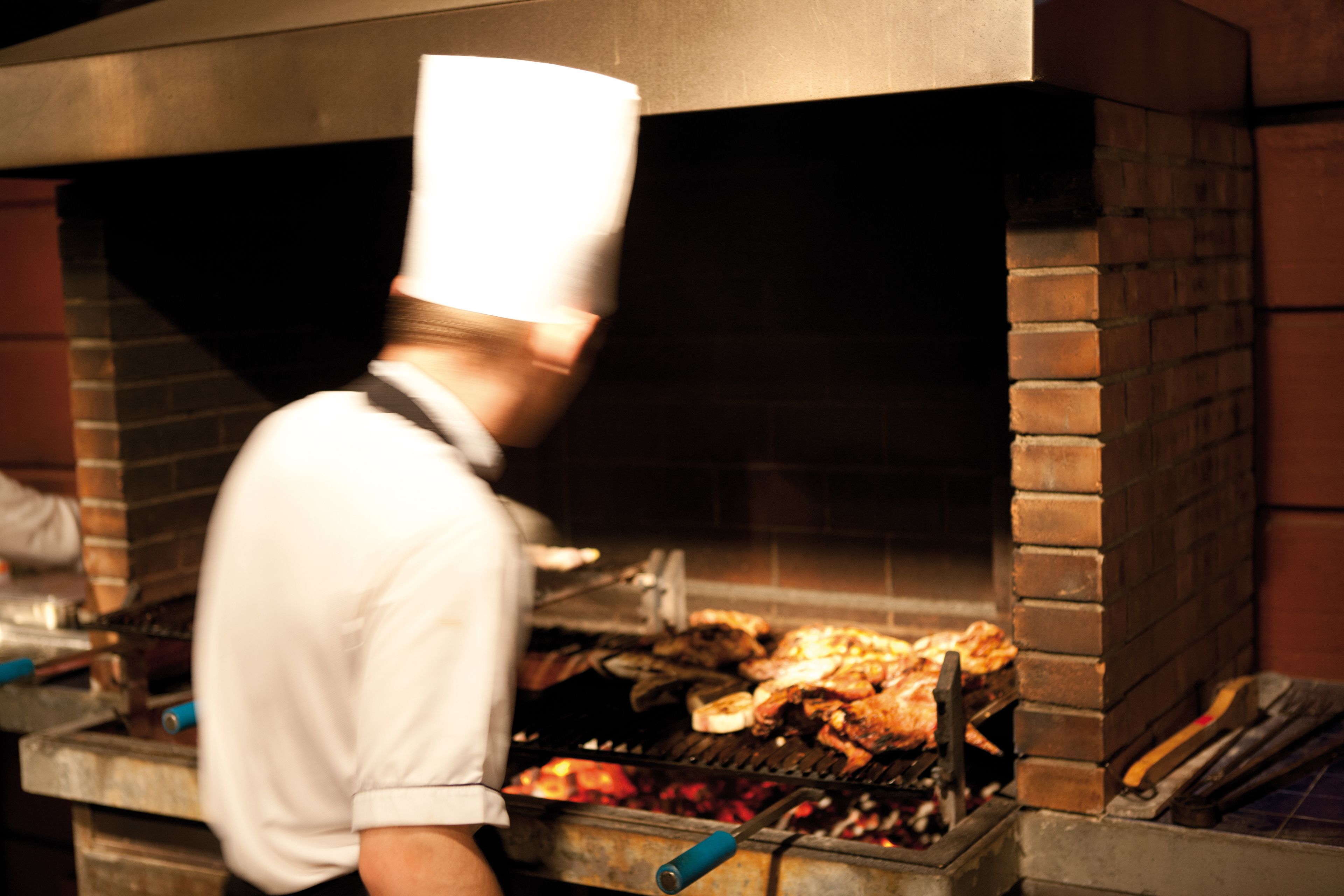 A chef in a white uniform and tall hat cooking in a brick oven.