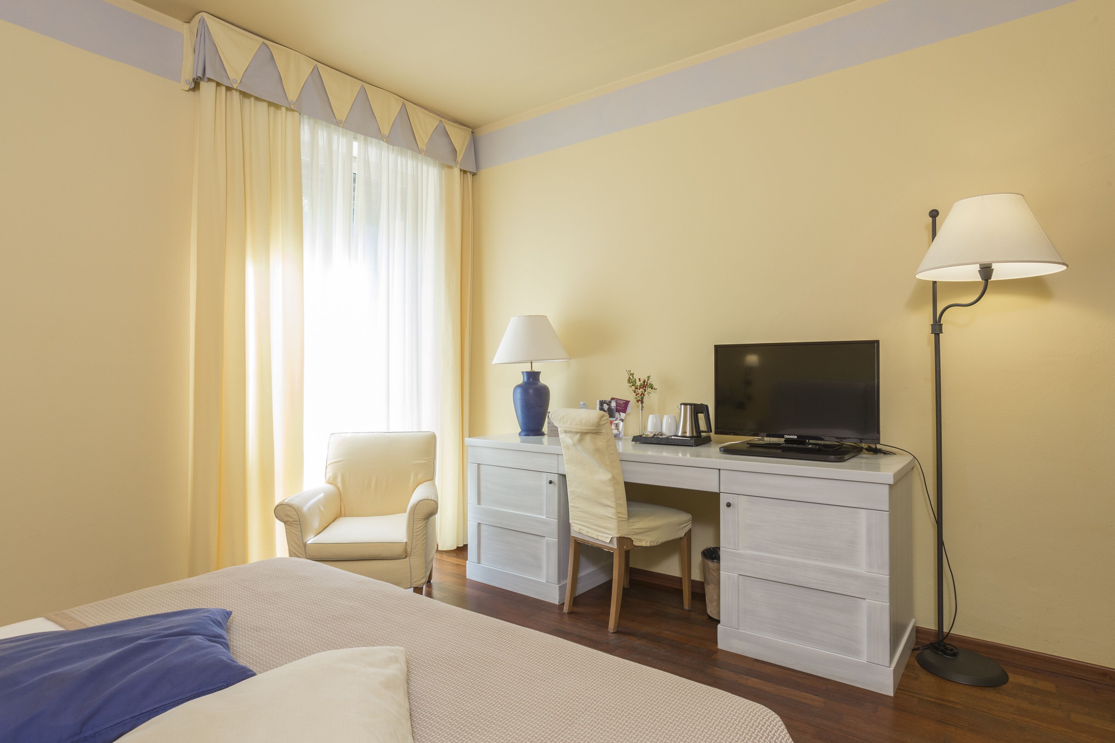 Una habitación de hotel con una cama, un escritorio con computadora, una silla, una lámpara y un televisor.