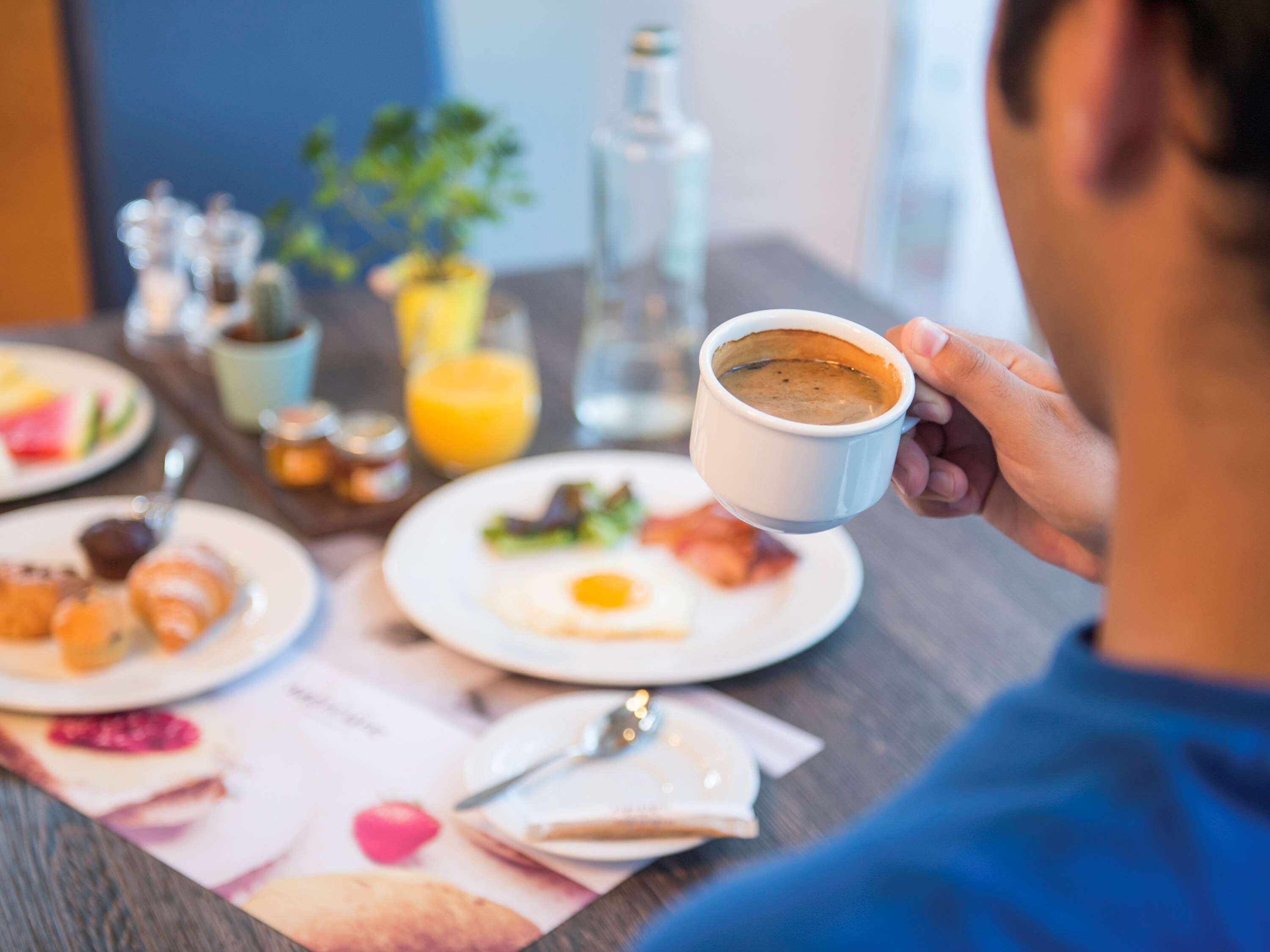 A breakfast setting with a cup of coffee, plates of food, and a menu.