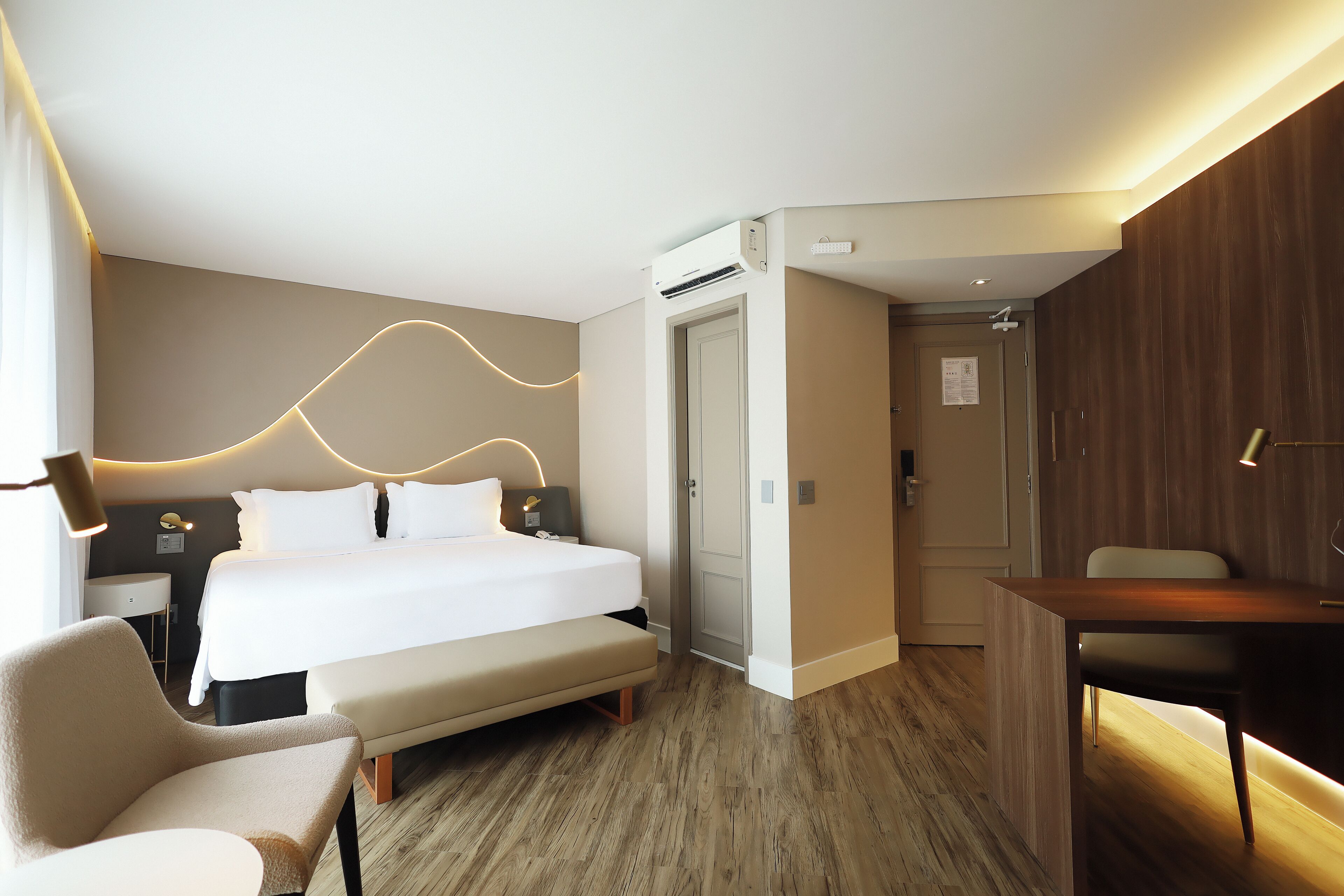 Quarto de hotel moderno com uma cama bem arrumada, uma escrivaninha e uma cadeira.