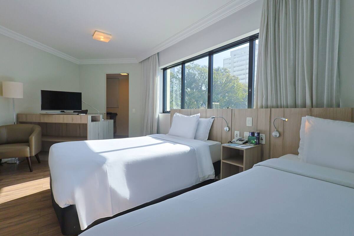 A hotel room with two beds, a desk with a television, and a window with curtains.