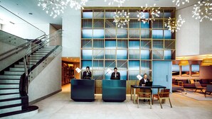Un moderno vestíbulo de hotel con escalera, mostrador de recepción, zona de estar y una gran pared con motivos geométricos.