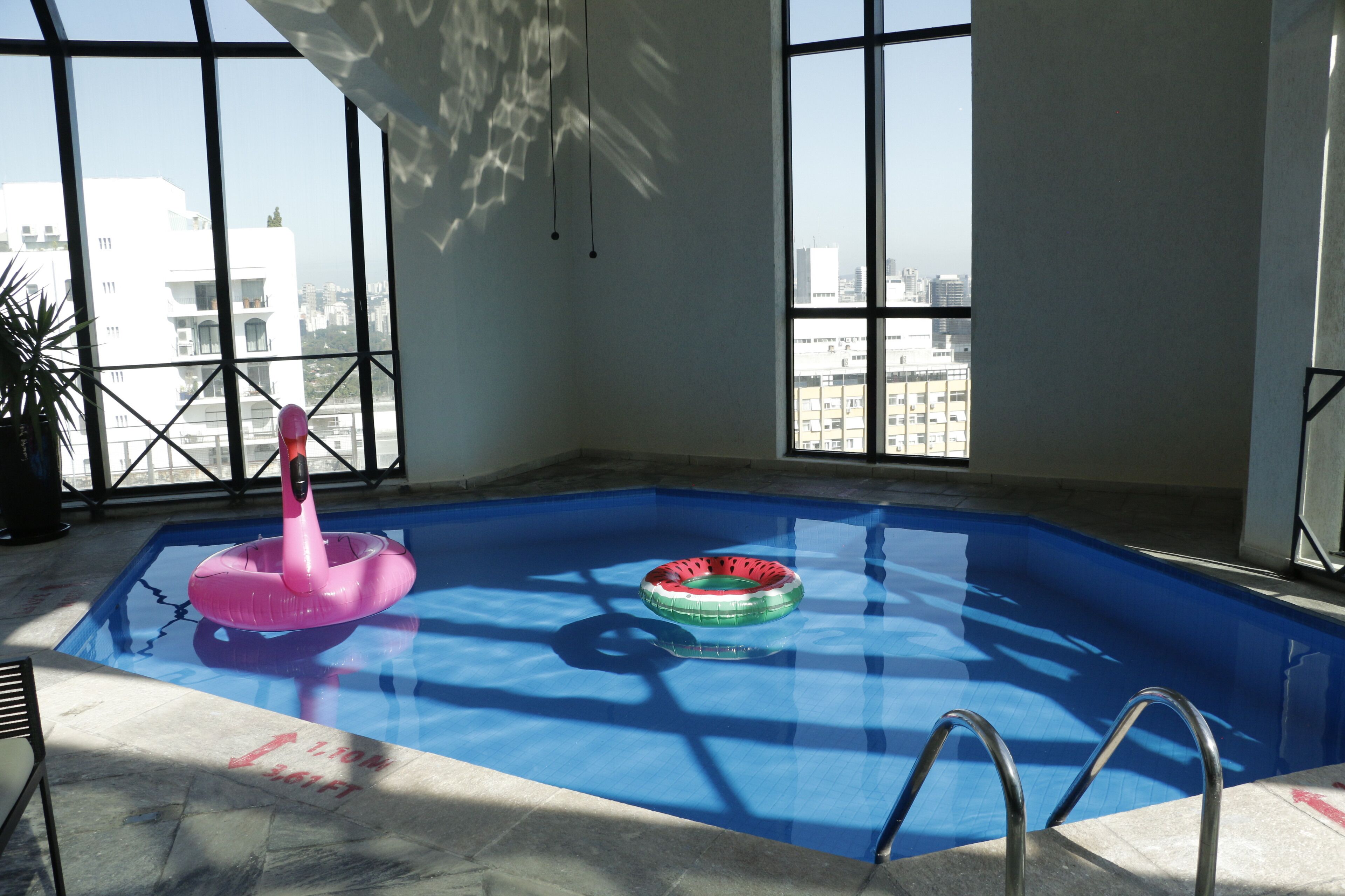 An indoor swimming pool with clear blue water, two inflatable rings, and a metal ladder.