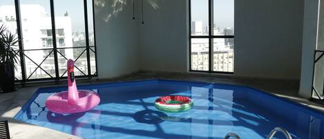 An indoor swimming pool with clear blue water, two inflatable rings, and a metal ladder.