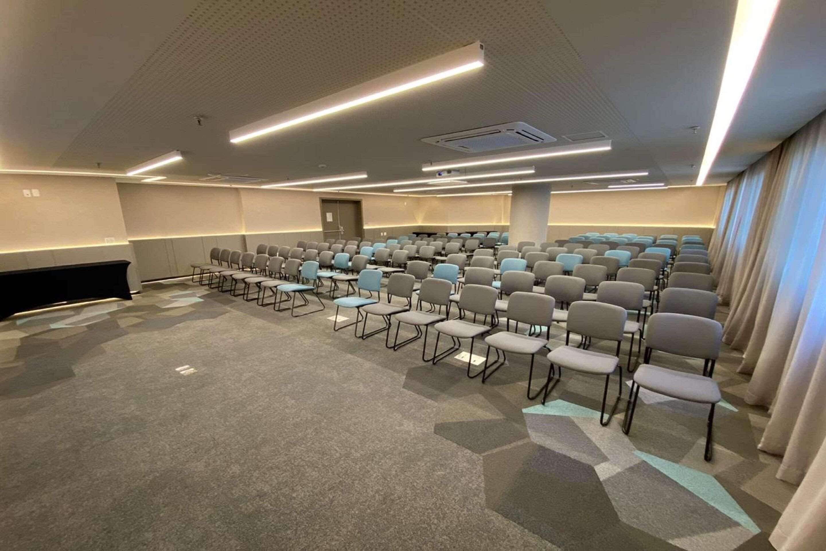 A conference room with rows of chairs, a stage, and a carpeted floor.